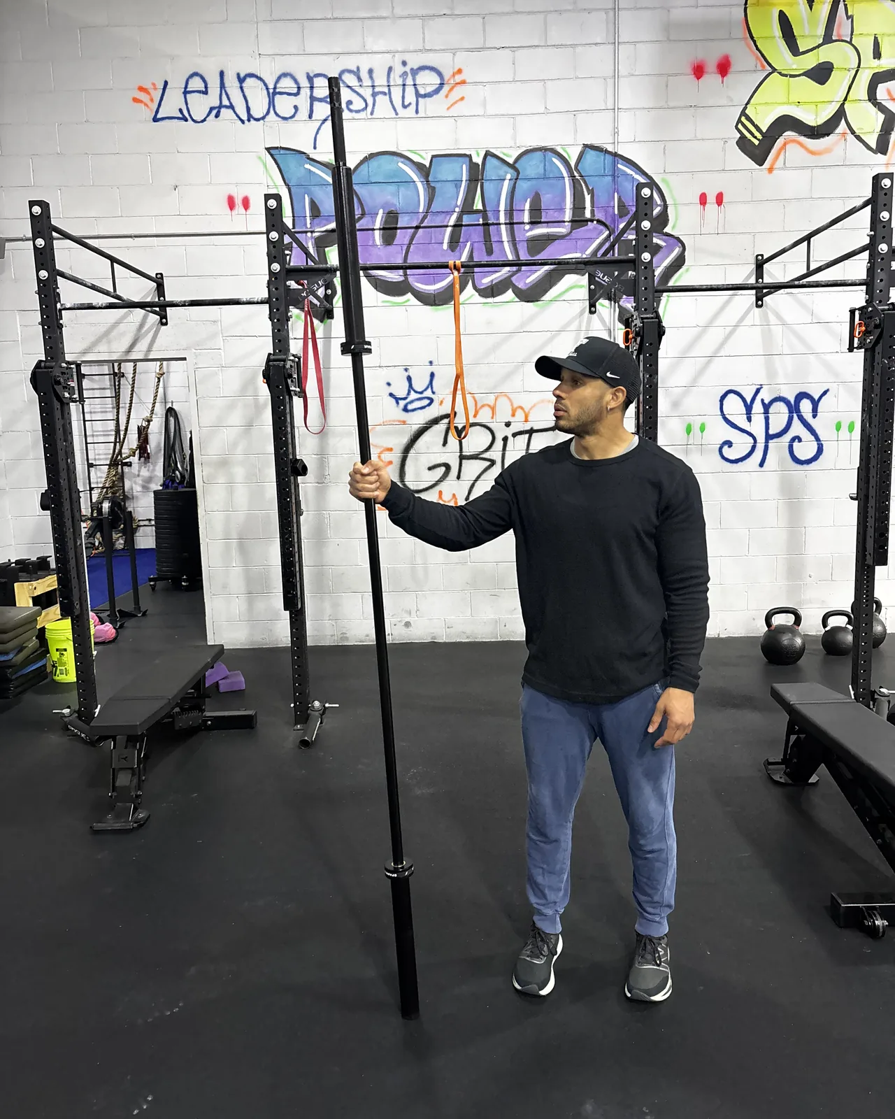 A coach holding the Spann Bar upright on the floor at SPS Fit, in front of the Leadership, Power, Grit wall.